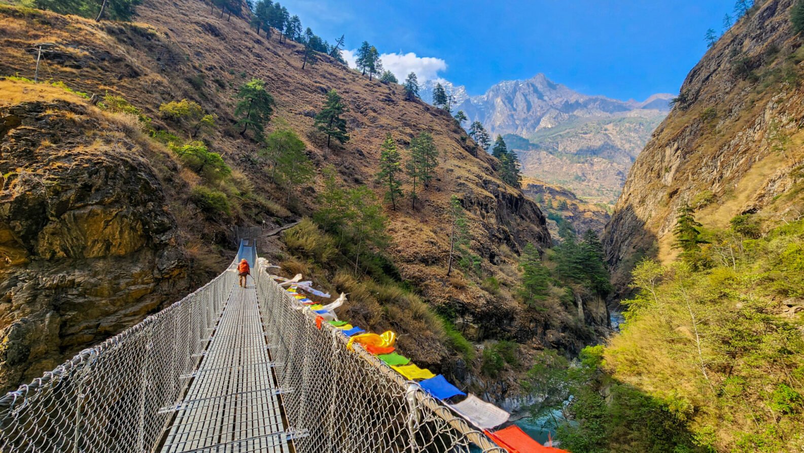 Pont suspendu traversant une gorge profonde, bordé de drapeaux de prières multicolores