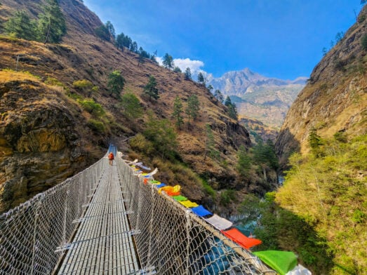 Pont suspendu traversant une gorge profonde, bordé de drapeaux de prières multicolores