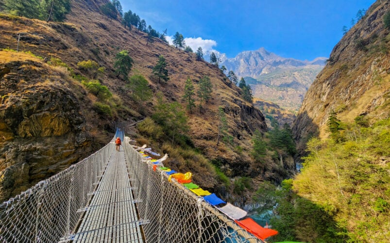 Pont suspendu traversant une gorge profonde, bordé de drapeaux de prières multicolores