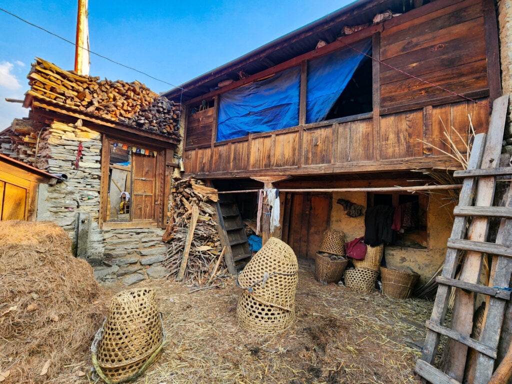 Maison traditionnelle en bois et paniers de récolte empilés au pied de l’habitation