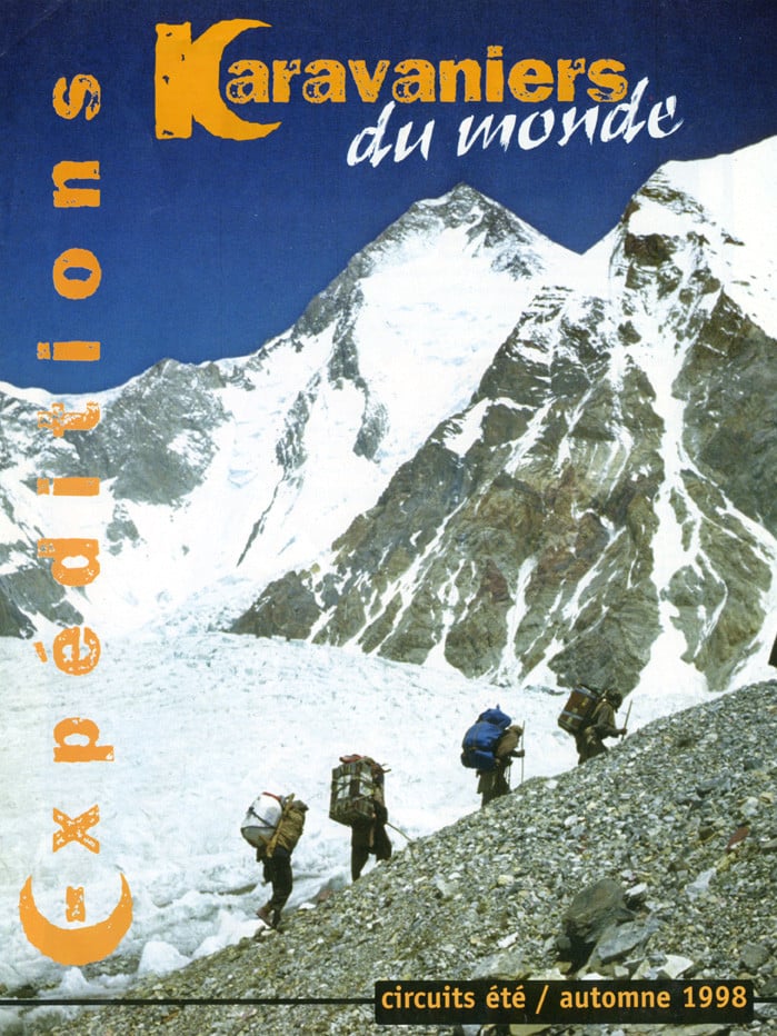 Couverture d’un ancien catalogue Karavaniers du Monde datant de l’été-automne 1998, montrant quatre trekkeurs lourdement chargés, progressant sur une pente rocailleuse au pied de hauts sommets enneigés de l’Himalaya