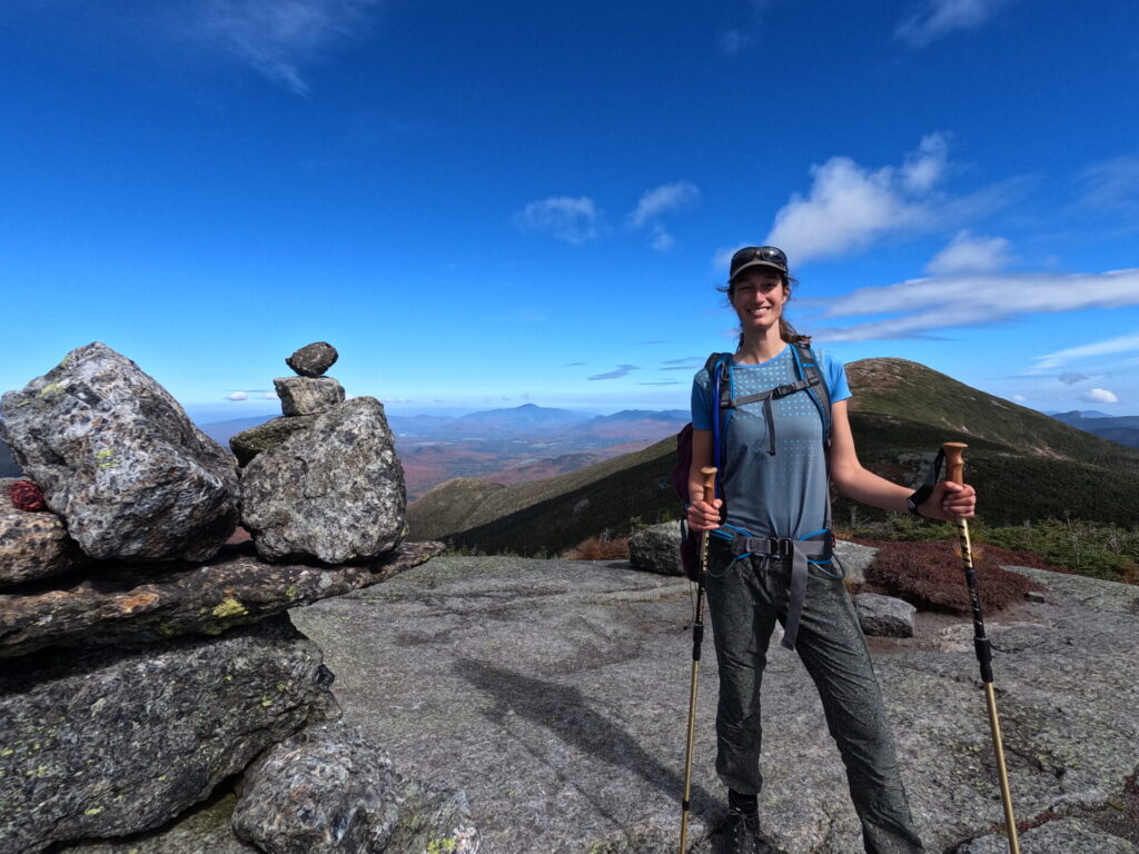 Malie Lessard Therrien, guide chez Karavaniers, qui pose sur le sommet d'une montagne rocheuse tenant des battons de randonnées dans les mains.