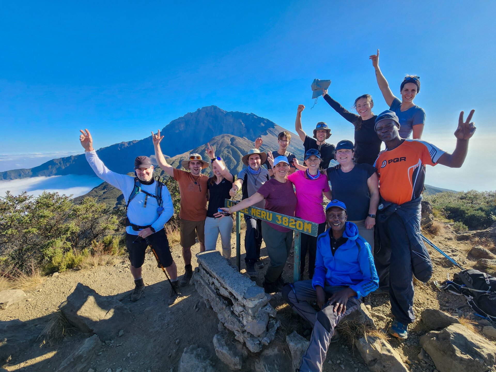 Groupe de voyageurs qui a terminé l'ascension du Mont Méru et pose devant le panneau, au sommet.