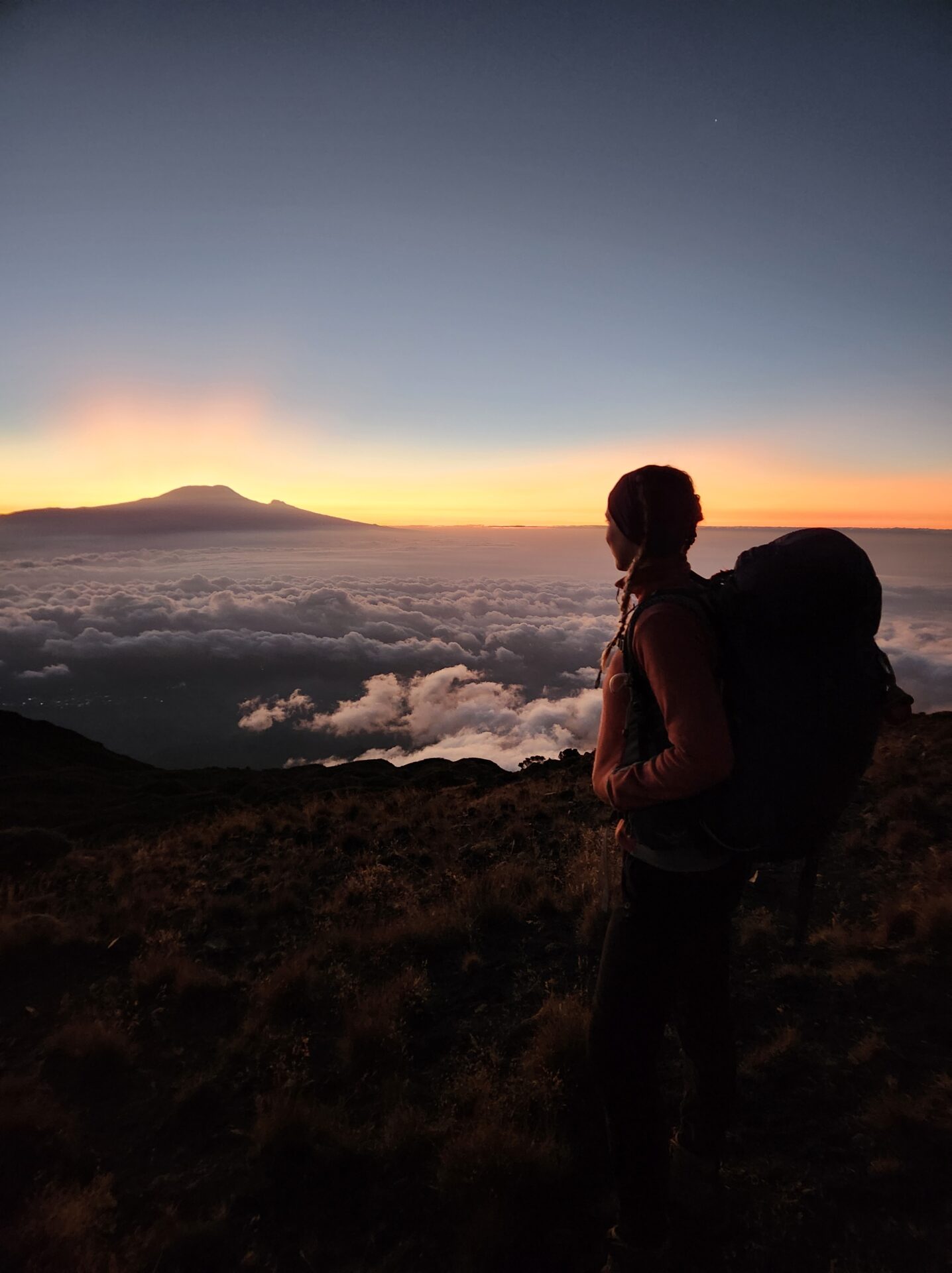 Randonneuse qui regarde au loin, par dessus les nuages, le Kilimandjaro qui dépasse. Le toit de l'Afrique s'impose, majestueux, depuis le Mont Méru.