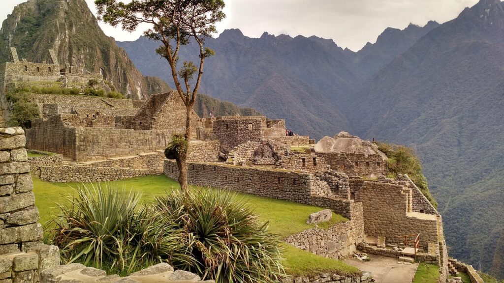 Les anciennes ruines de pierre du Machu Picchu se trouvent au sommet d'une montagne verdoyante, entourées de plantes luxuriantes et de pics brumeux. C'est une récompense à couper le souffle pour ceux qui parcourent le camino Inca au Pérou sous un ciel nuageux. - Karavaniers