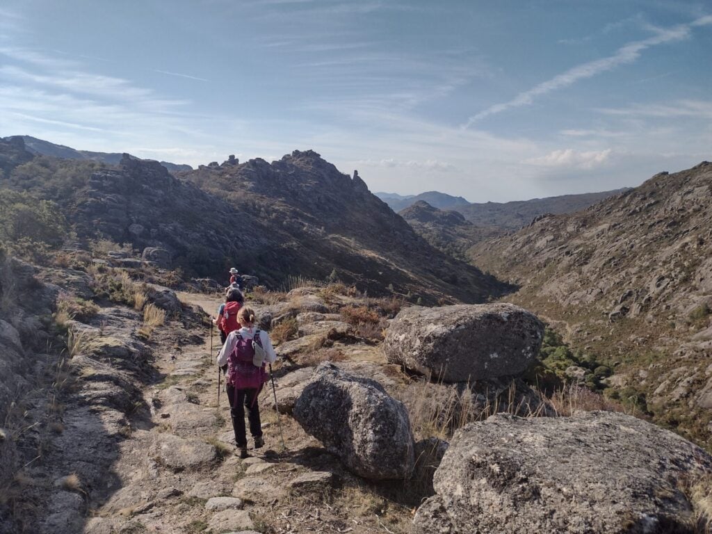 Un groupe de randonneurs munis de sacs à dos et de bâtons suit un sentier rocailleux à travers un paysage montagneux sous un ciel partiellement nuageux, profitant d'une randonnée près des châteaux de Peneda. - Karavaniers