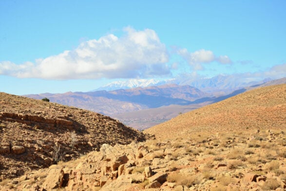Un paysage désertique sec et rocailleux avec une végétation clairsemée au premier plan, des collines en pente et des montagnes enneigées au loin sous un ciel bleu partiellement nuageux - une scène impressionnante d'un voyage au Monténégro. - Karavaniers