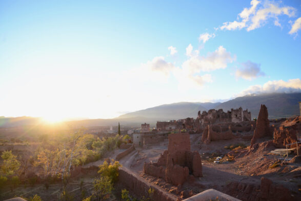 L'image évoque un Voyage au Monténégro, avec les ruines de vieux bâtiments en pisé dans un paysage désertique au coucher du soleil. Des montagnes et des nuages encadrent l'arrière-plan, tandis que la lumière du soleil provenant de la gauche éclaire partiellement cette scène évocatrice. - Karavaniers