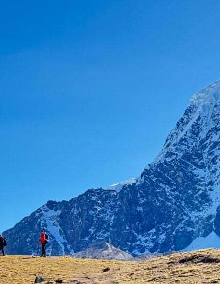 Cinq personnes se promènent dans une plaine herbeuse avec, en arrière-plan, un pic montagneux enneigé et un ciel bleu limpide - une scène incontournable pour tout amoureux de la nature après une conférence ou une retraite. - Karavaniers