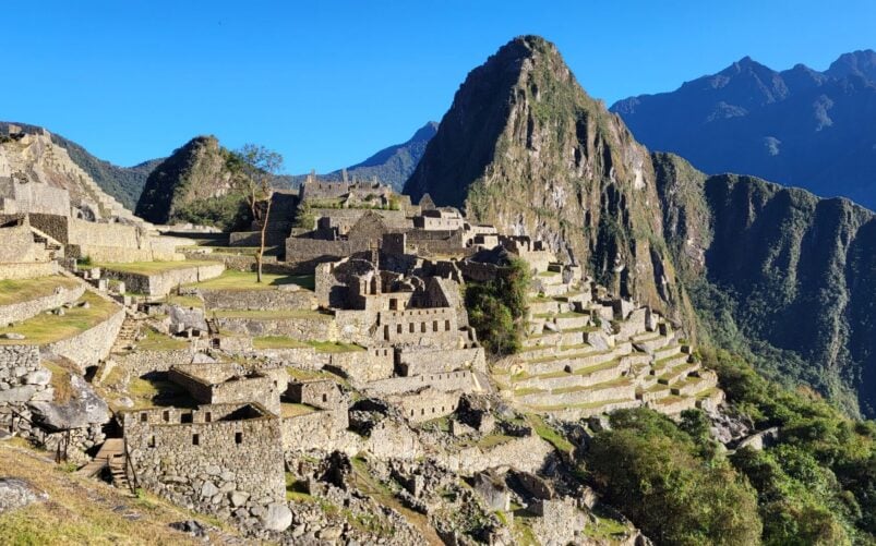 Vue sur le Machu Picchu, une ancienne citadelle inca située au Pérou, avec ses constructions en pierre, ses terrasses et ses montagnes verdoyantes sous un ciel bleu limpide : un site à couper le souffle, idéal pour toute conférence sur l'histoire ou la culture. - Karavaniers