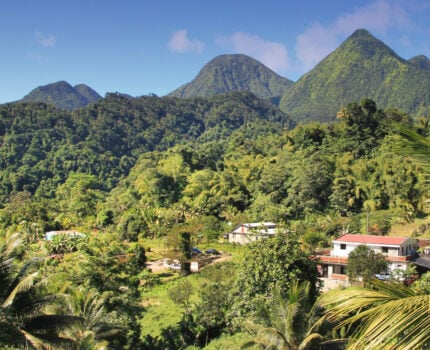 Un village dont les maisons sont nichées dans une vallée montagneuse verdoyante, au pied de sommets imposants recouverts de forêts, lors d'un trek en République Dominicaine. - Karavaniers