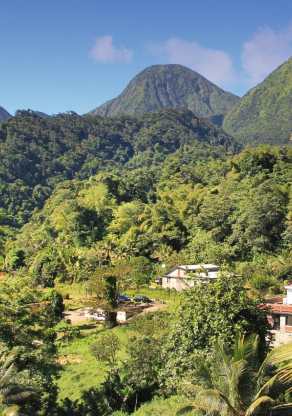 Un village dont les maisons sont nichées dans une vallée montagneuse verdoyante, au pied de sommets imposants recouverts de forêts, lors d'un trek en République Dominicaine. - Karavaniers