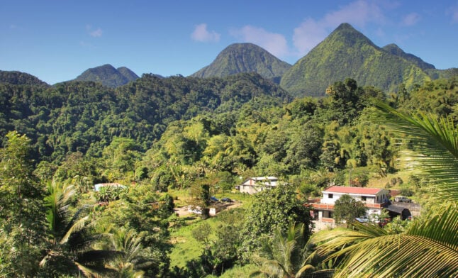 Un village dont les maisons sont nichées dans une vallée montagneuse verdoyante, au pied de sommets imposants recouverts de forêts, lors d'un trek en République Dominicaine. - Karavaniers