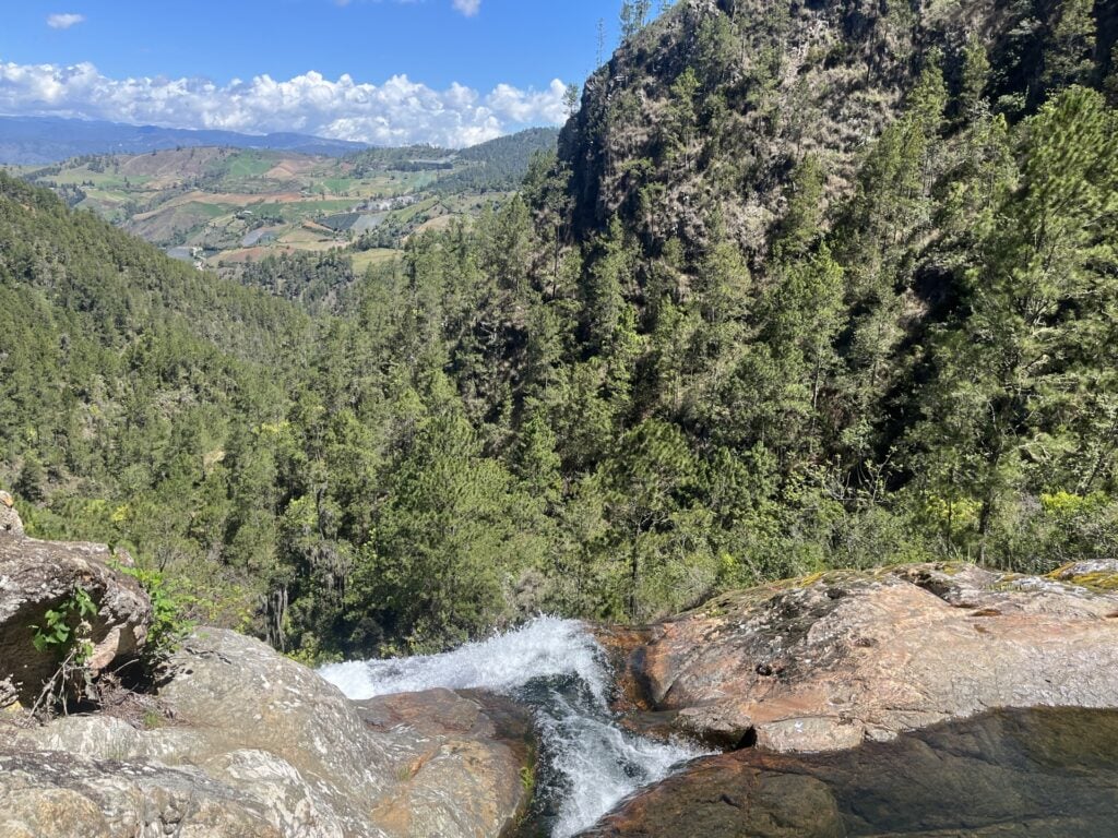 Une cascade dévalant une corniche rocheuse pour se jeter dans une vallée boisée et luxuriante, lors d'une randonnée en République Dominicaine. - Karavaniers