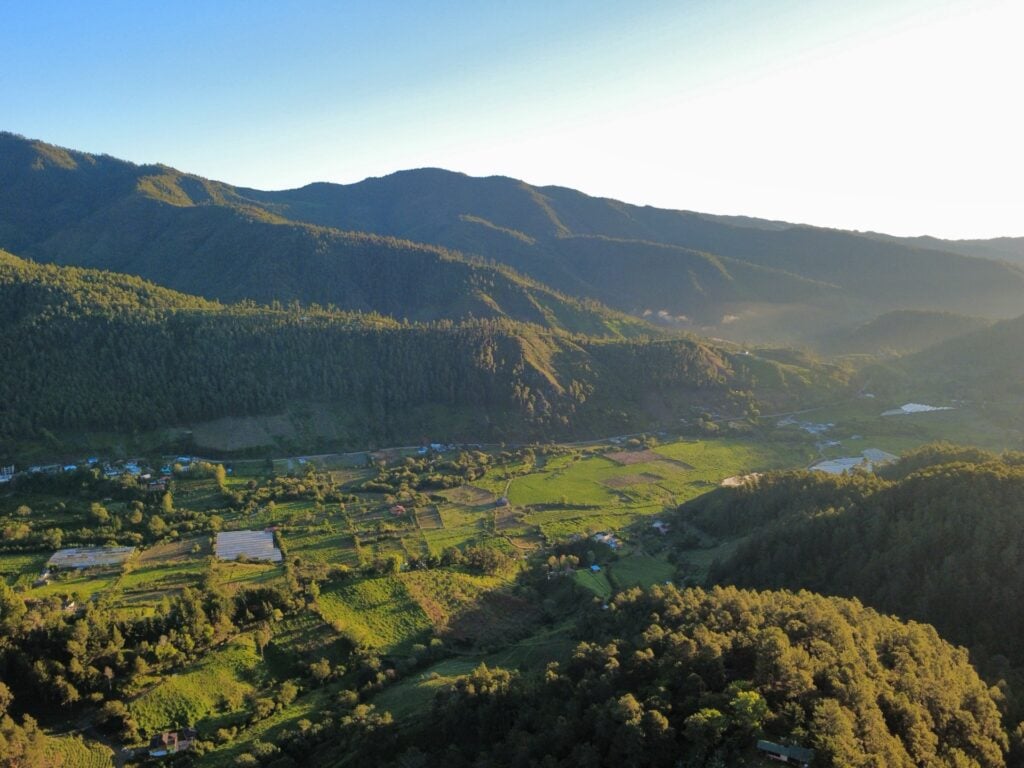 Une vue aérienne d'une vallée verdoyante en République dominicaine, idéale pour une randonnée, entourée de montagnes boisées sous un ciel radieux. - Karavaniers